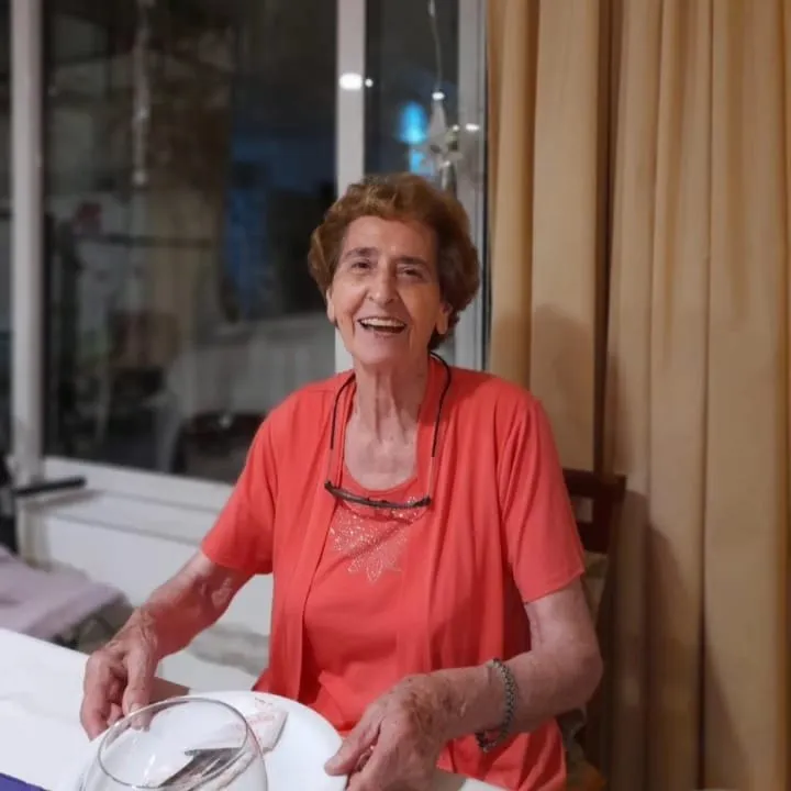 Una mujer mayor sonríe sentada a la mesa de su casa.