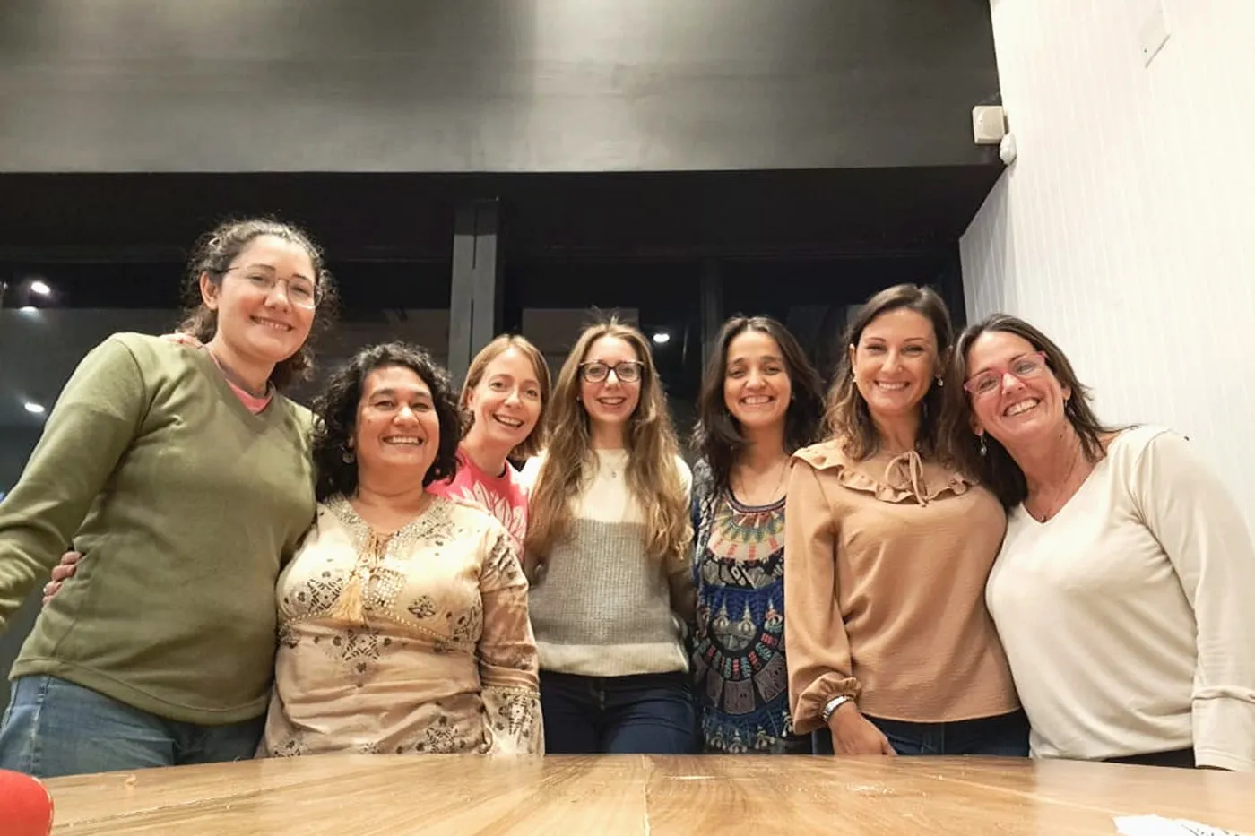 Siete integrantes del equipo de Ámbar, abrazadas y sonriendo, en un salón de encuentros.